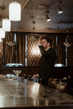 A man in a black suit drinks at a cozy bar with elegant decor. Perfect for leisure and lifestyle themes.