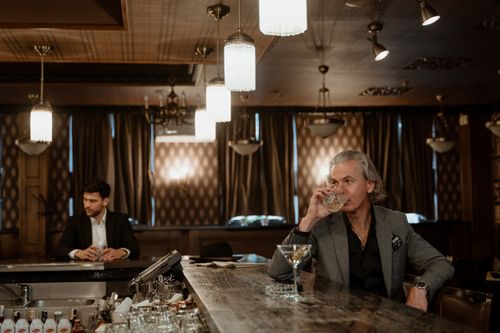 Free Two men enjoying drinks in a sophisticated bar with warm lighting and classic decor. Stock Photo