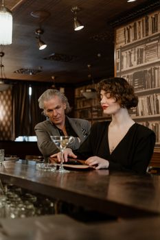 An elegant couple enjoying drinks at a sophisticated bar with vintage decor.