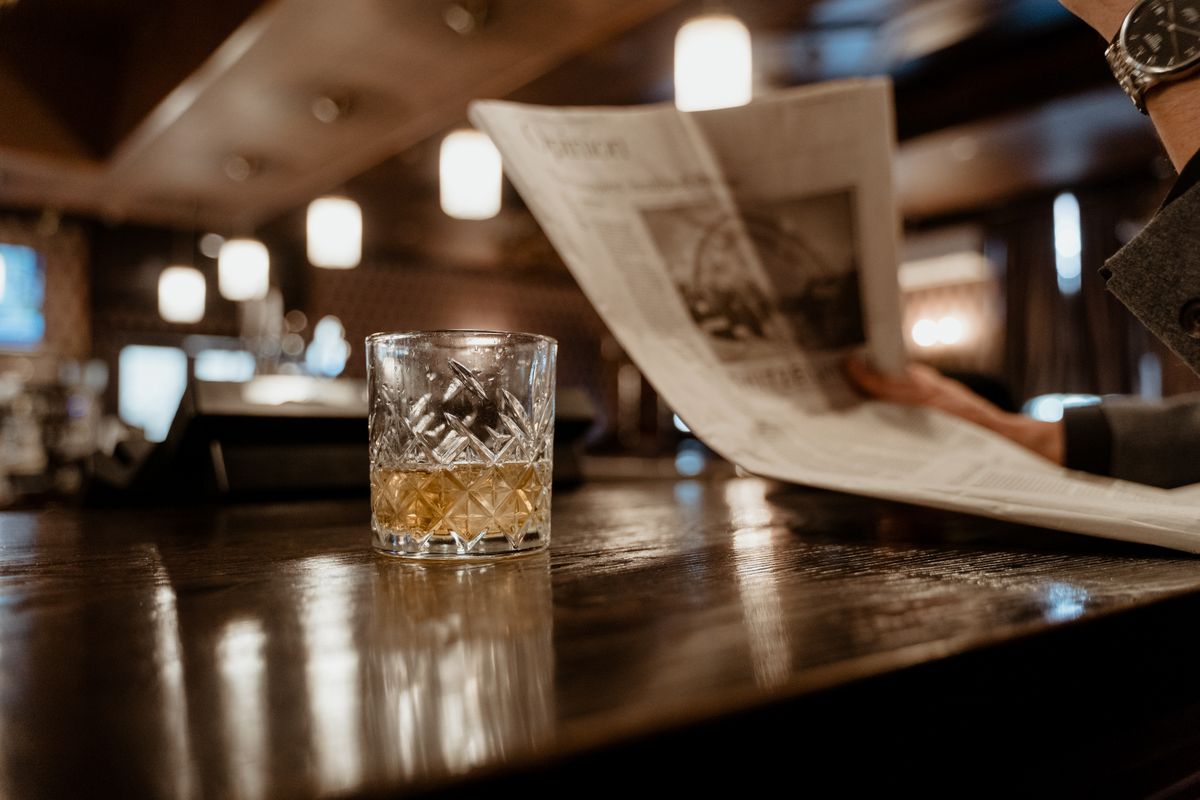 A glass of whiskey resting on a wooden bar counter in low light