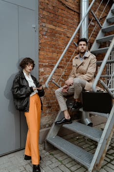Stylish man and woman in retro outfits posing near industrial stairs outdoors.