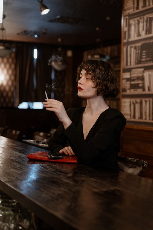 Free Elegant woman smoking in a dimly lit bar setting, exuding a cinematic vibe. Stock Photo
