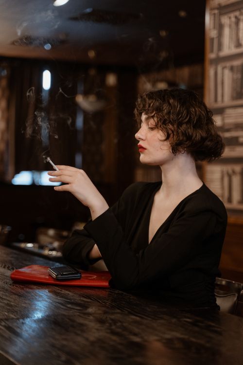 Free Sophisticated woman with short hair smoking in a vintage bar setting. Classic and stylish atmosphere. Stock Photo