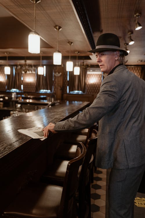 A Man in Gray Suit and Black Hat Standing Beside Bar Counter