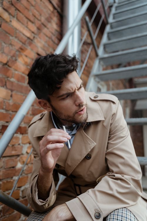 Free A man in a trench coat sitting on outdoor stairs with a thoughtful expression. Stock Photo