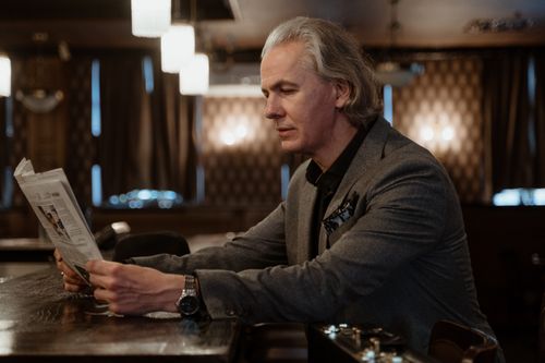 Free Mature businessman in gray suit reading newspaper at a cozy bar. Stock Photo