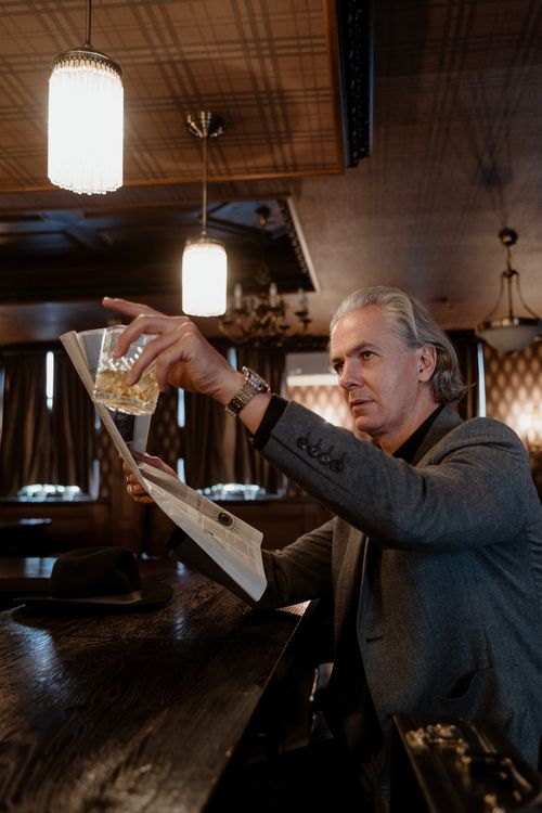 Free Elegant senior man reading a newspaper while savoring whiskey in a classic bar setting. Stock Photo