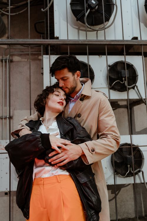 Free Couple embracing against industrial backdrop, showcasing love and fashion. Stock Photo