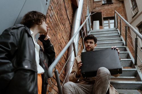 Free Stylish duo in an urban setting, showcasing retro fashion with a briefcase and leather jacket. Stock Photo