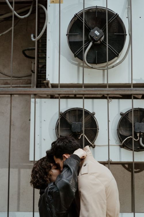 Free A couple shares an affectionate moment near industrial fans, symbolizing love in urban settings. Stock Photo