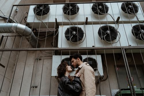 Free A stylish couple shares an intimate moment near industrial air conditioning units. Stock Photo