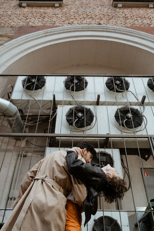 Free Couple embracing outdoors by industrial air vents with a rustic brick backdrop. Stock Photo