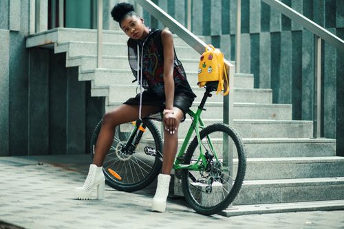 Free Stylish black woman posing outdoors with a bicycle on stone stairs, showcasing fashion and urban lifestyle. Stock Photo
