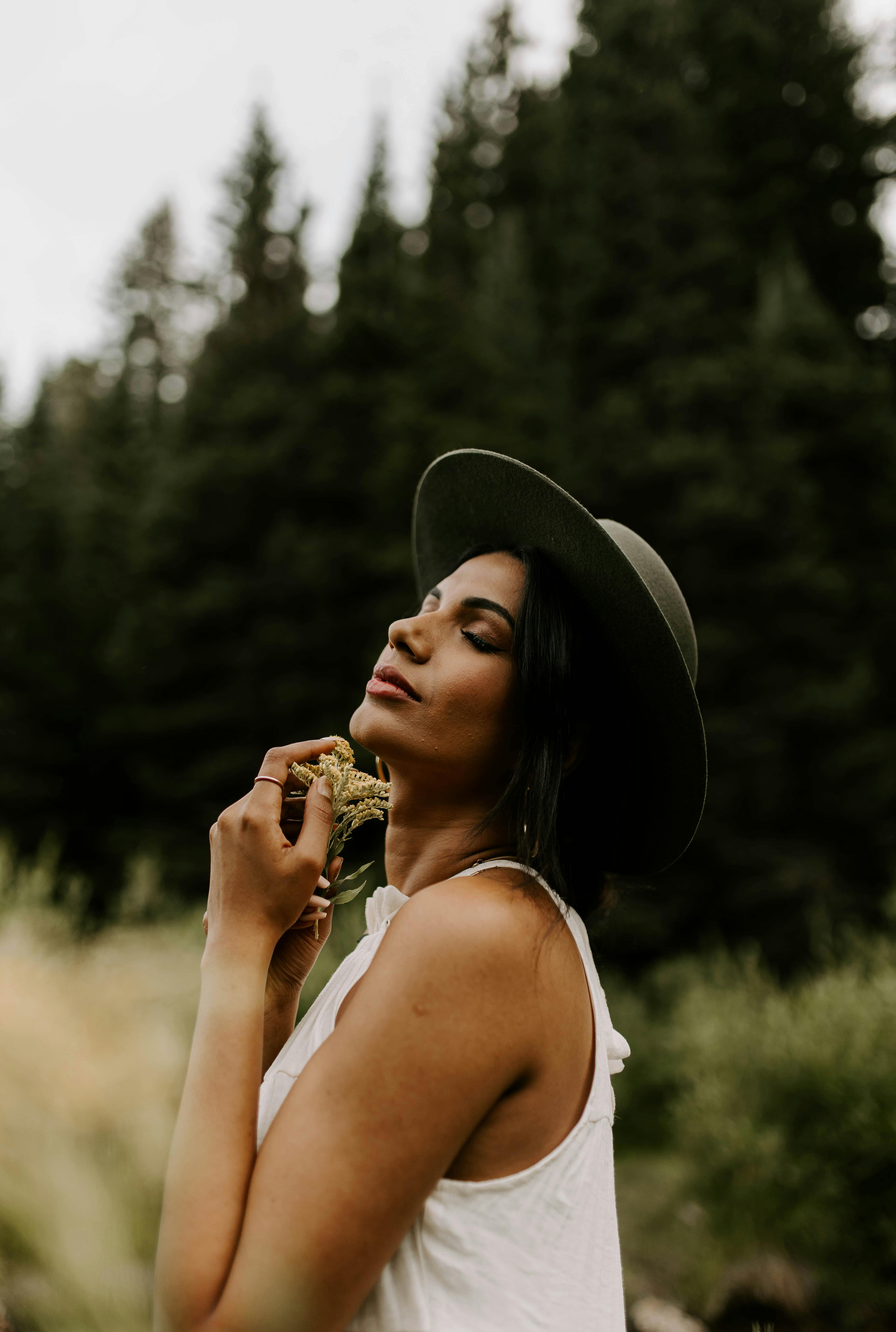 Portrait of a stylish woman with eyes closed, embracing nature in a forest setting.