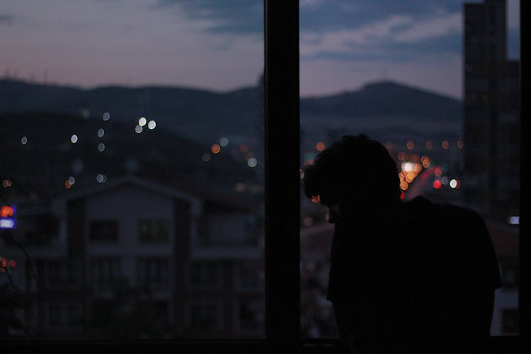 Silhouette Of A Man Looking At The Window At Night