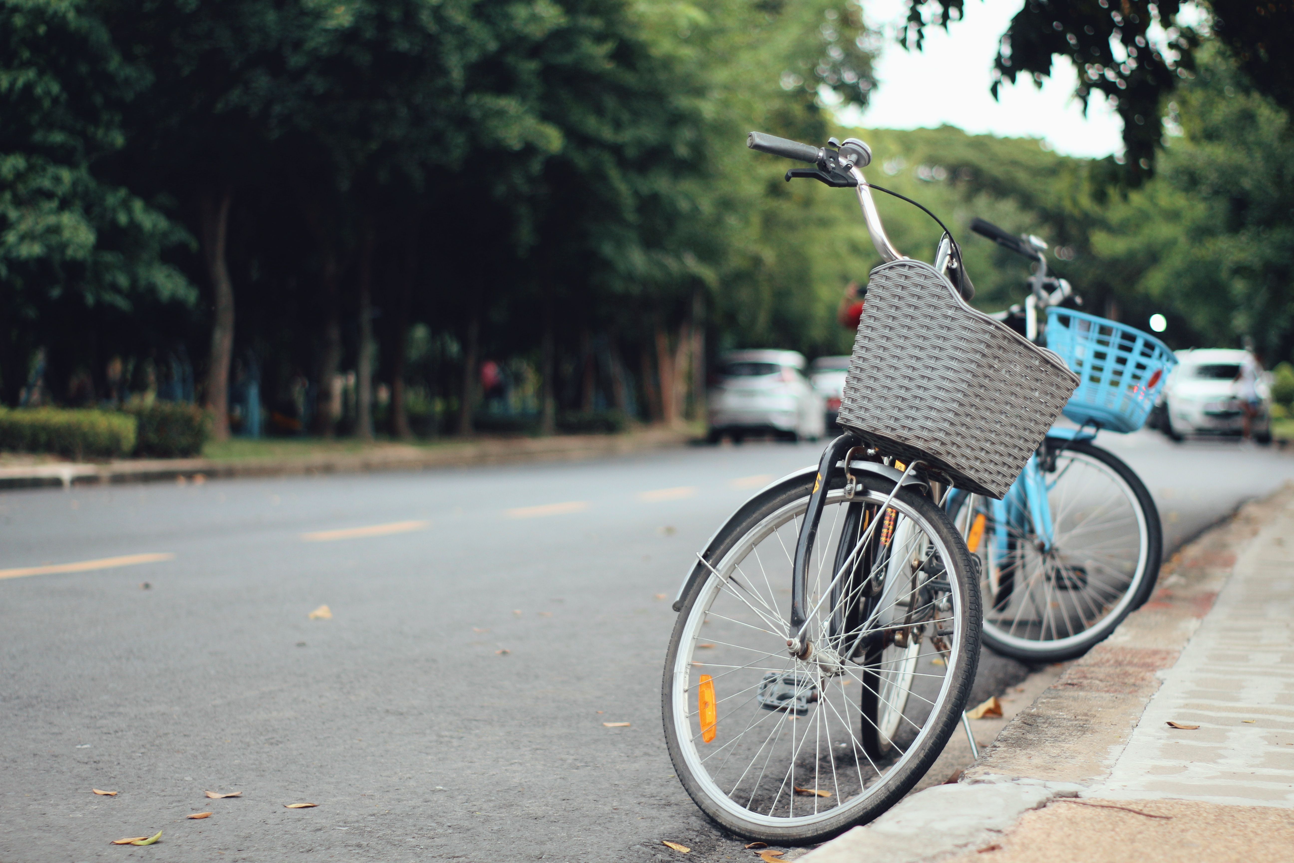 Two bicycles with baskets parked along a serene urban street, captured on a sunny day.