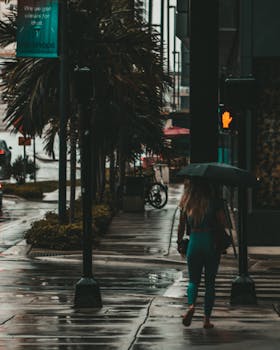 A woman with an umbrella navigates a rainy street, highlighting urban life during wet weather.