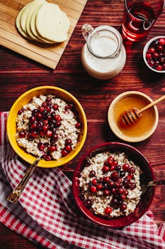 Top view of cranberry oatmeal bowls with honey and milk on a wooden table.