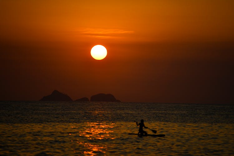 Silhouette Of Person Using A Paddle Board In The Sea During Sunset