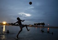 Man in Shorts Kicking a Ball on Water during Sunset