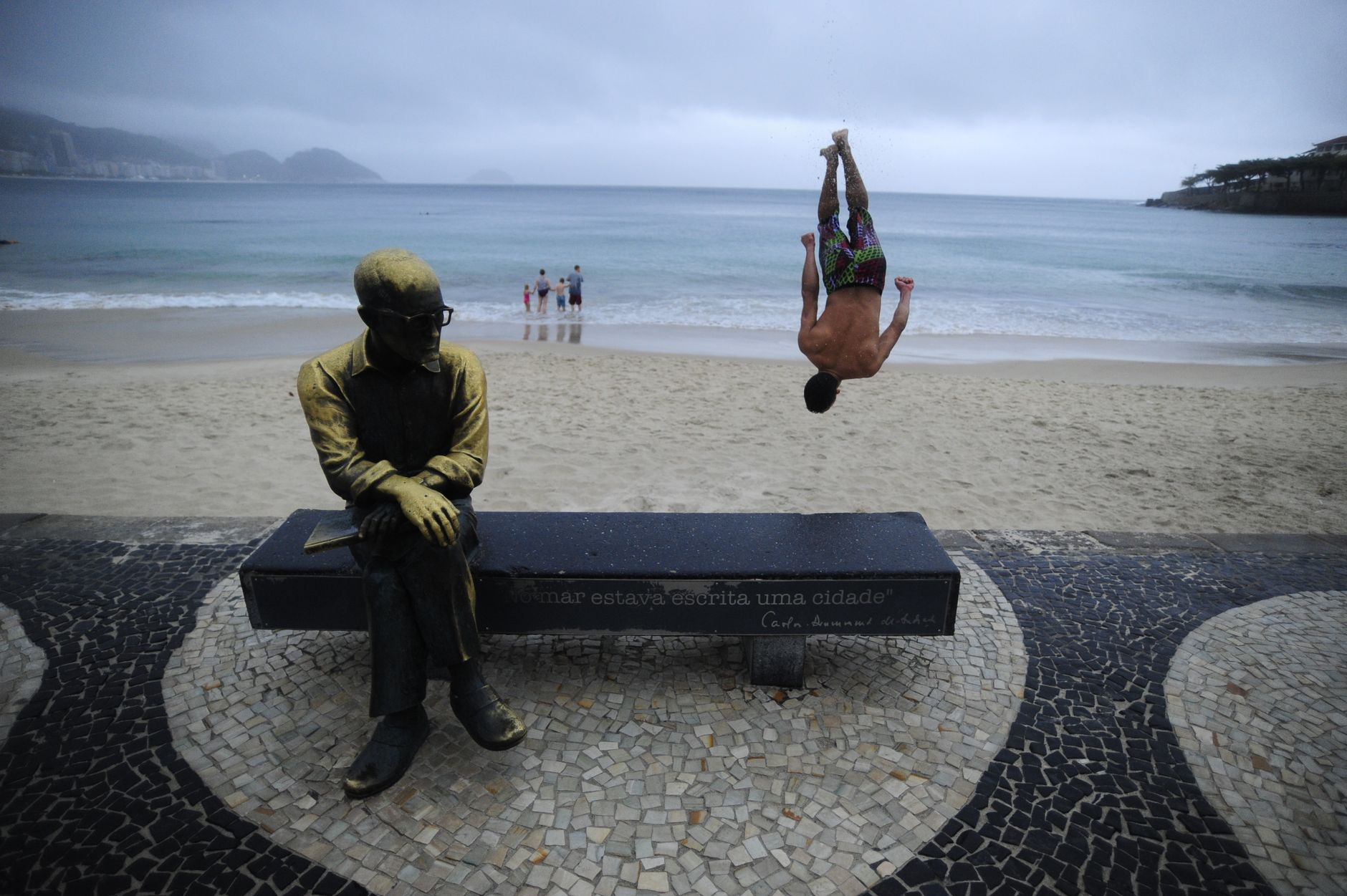 Street performer doing a flip near the Carlos Drummond statue at a Rio beach.