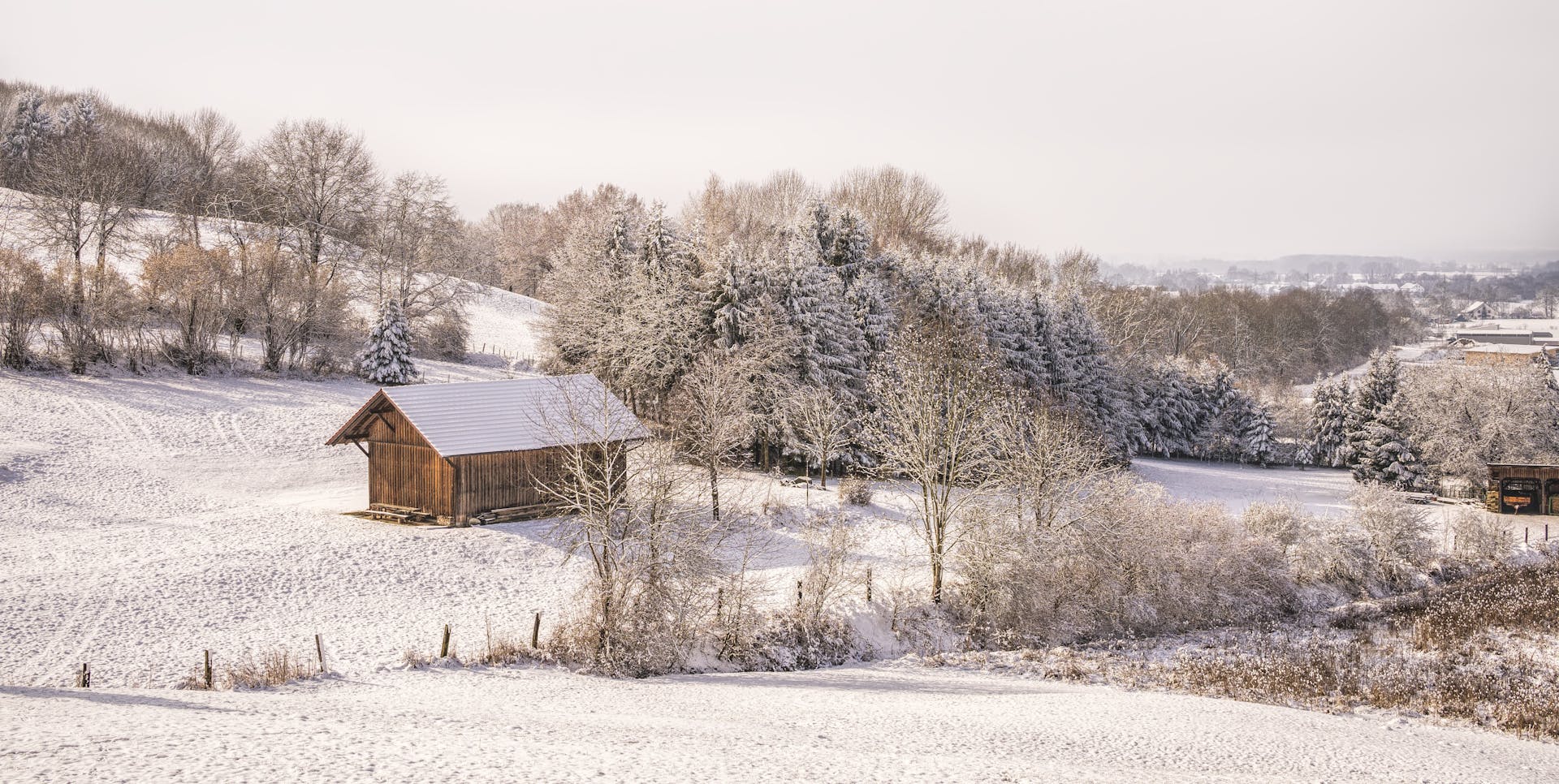 A tranquil snowy landscape featuring a wooden cabin and a frosty forest in winter.