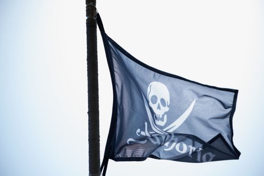 Close-up of a pirate flag with skull waving against the sky.