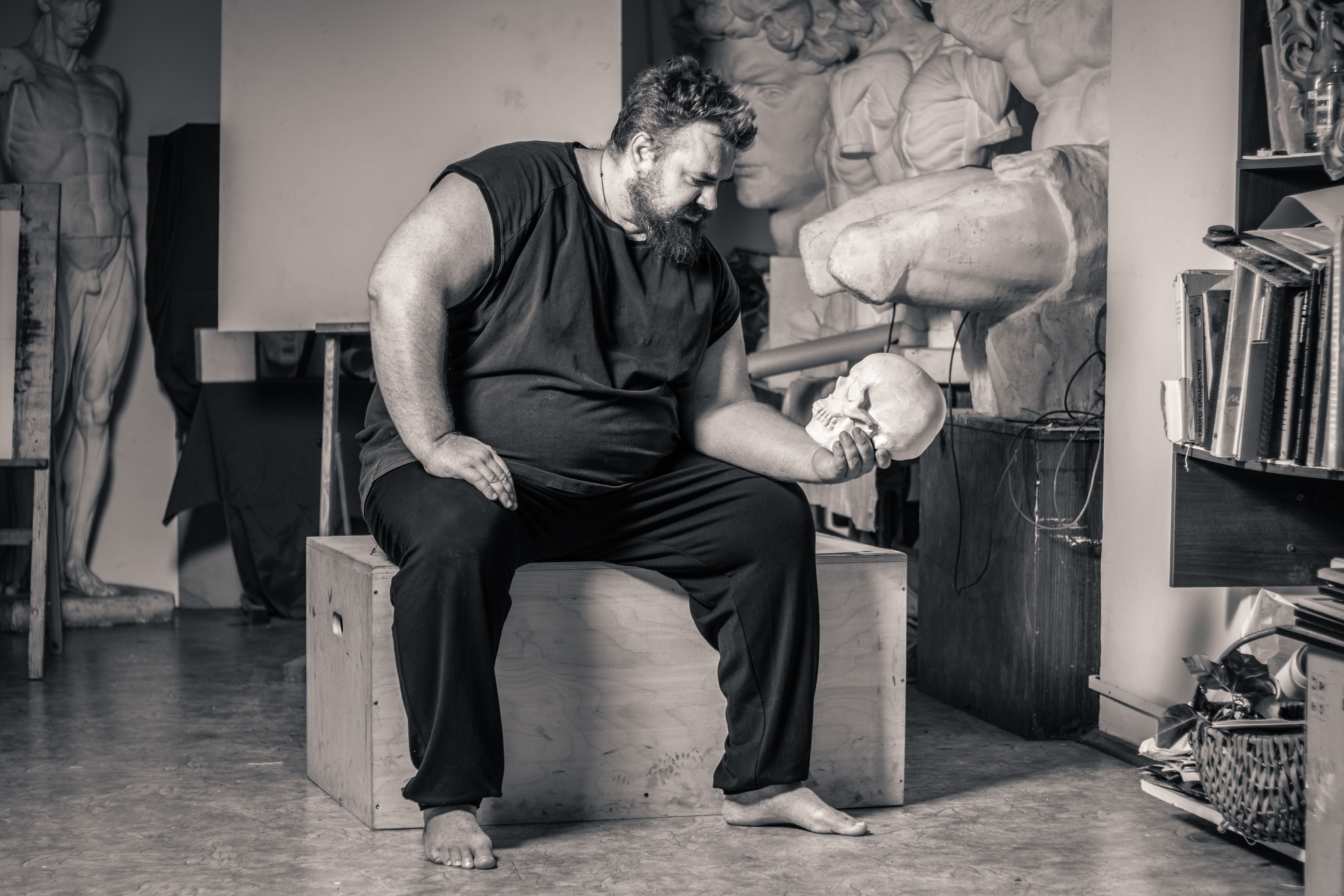 Plus-size man contemplating a skull in an art studio, evoking introspection and creativity.