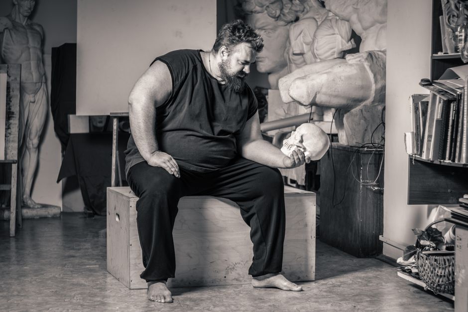Plus-size man contemplating a skull in an art studio, evoking introspection and creativity.