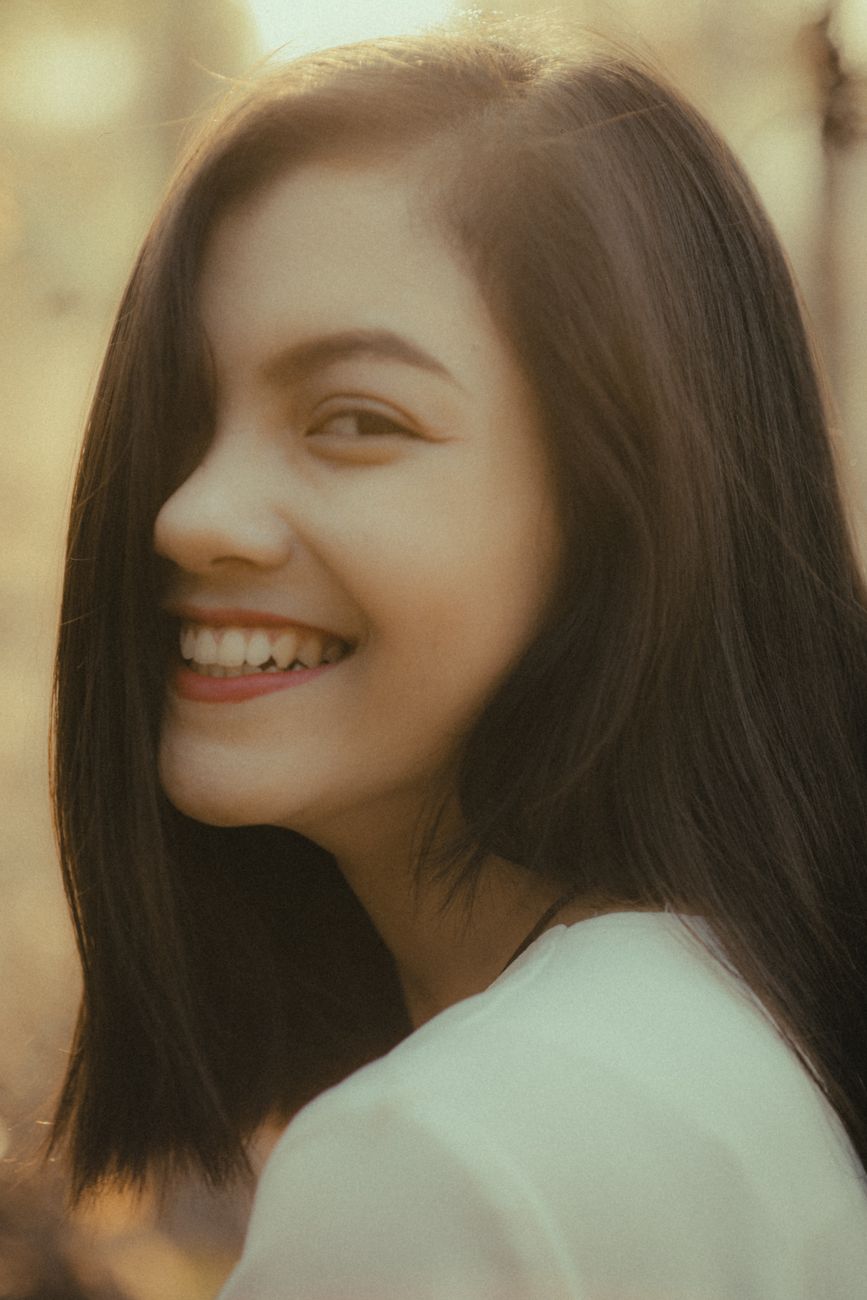 Portrait of a young woman smiling warmly, captured in soft, golden natural light.