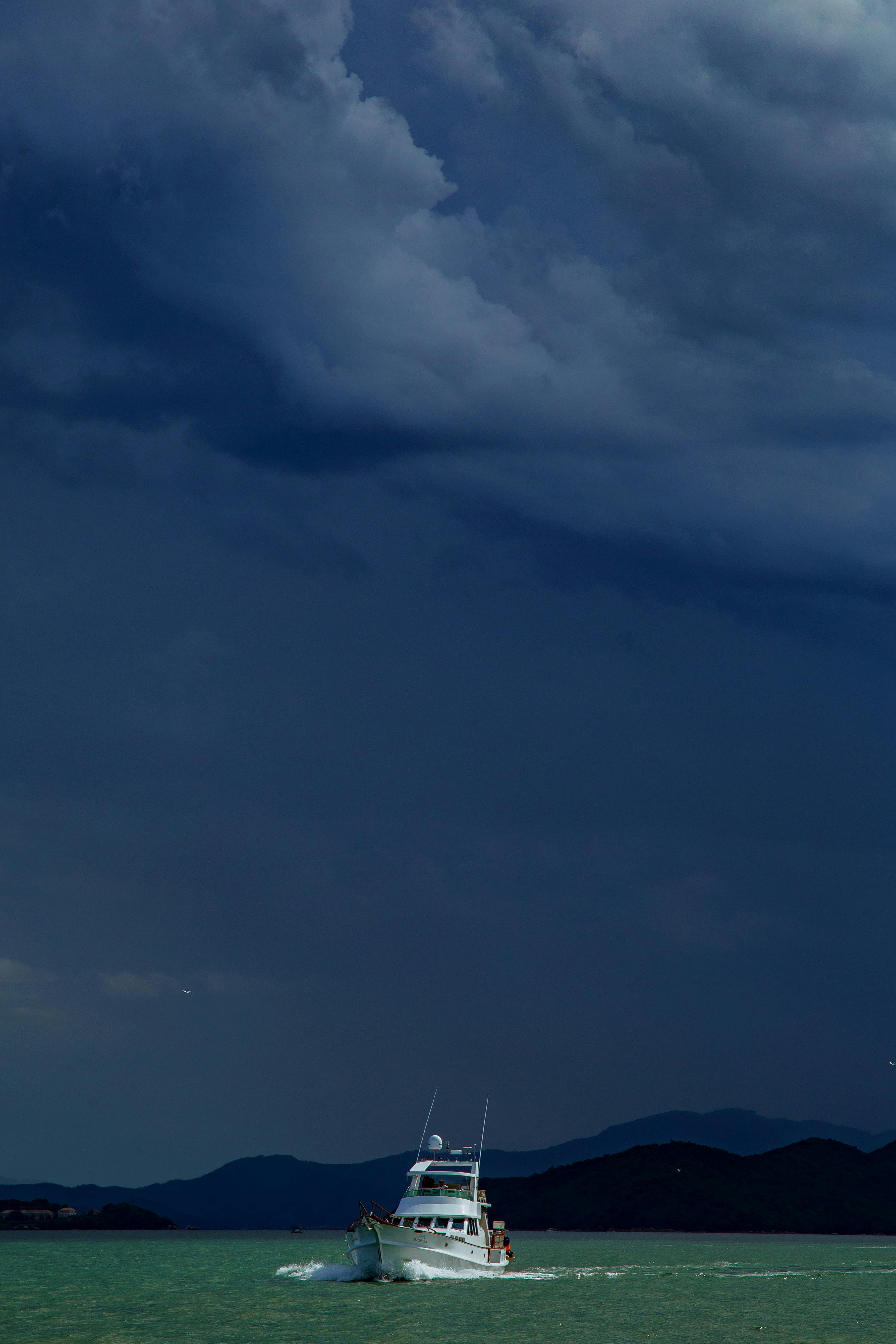Free A boat navigates through ocean waters under a dramatic, cloudy sky near mountain silhouettes. Stock Photo