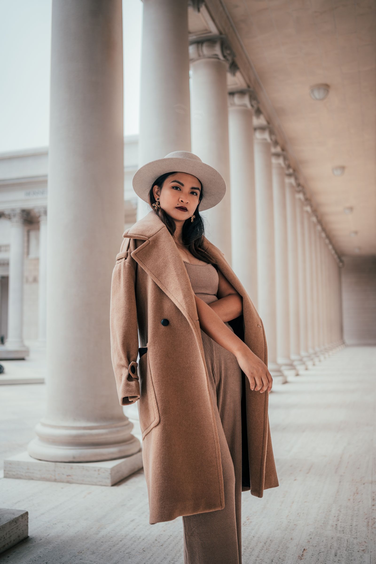 Woman in a camel wool coat and hat between stone columns
