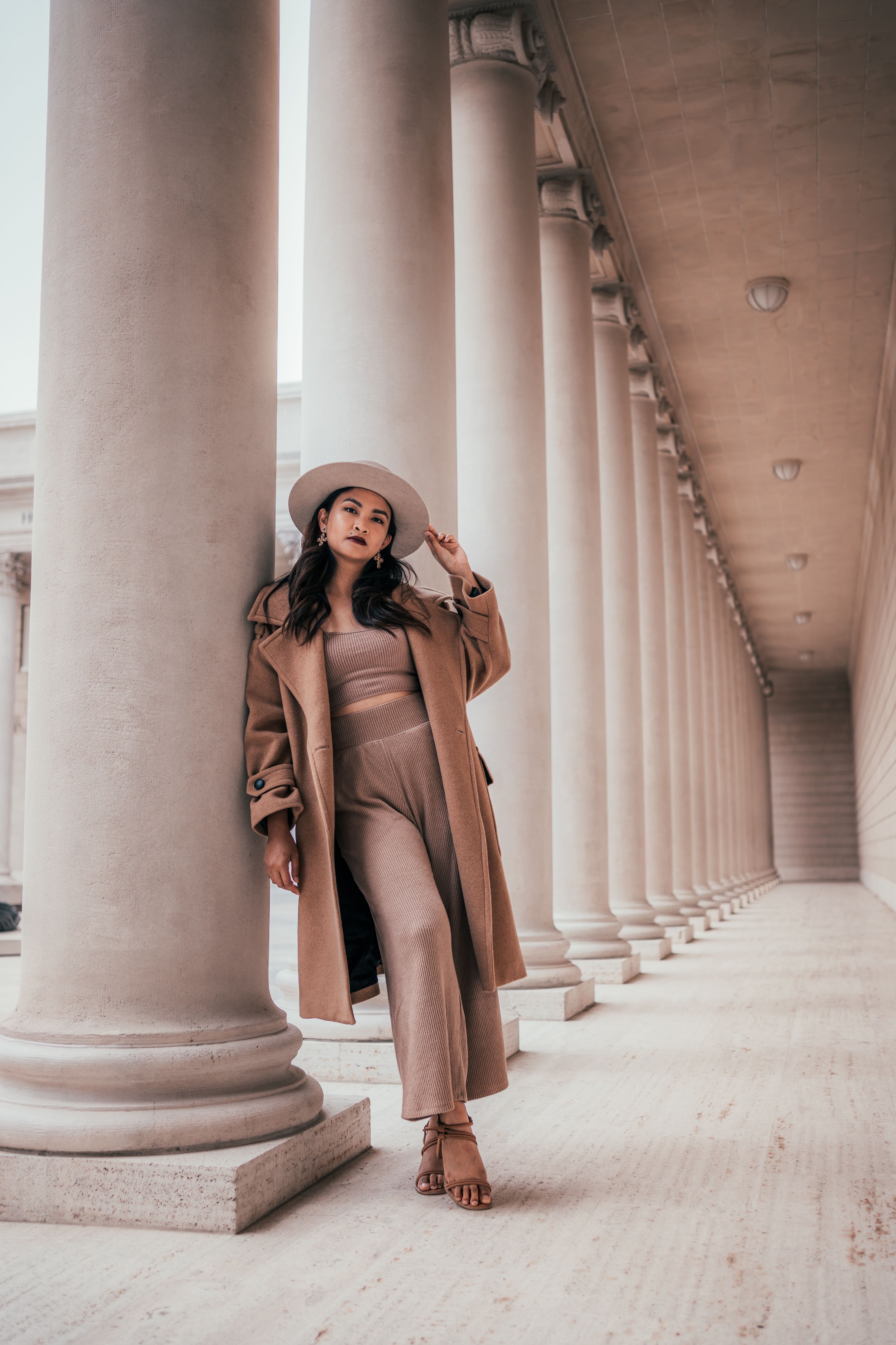 Woman in Brown Coat Standing on White Concrete Building · Free Stock Photo
