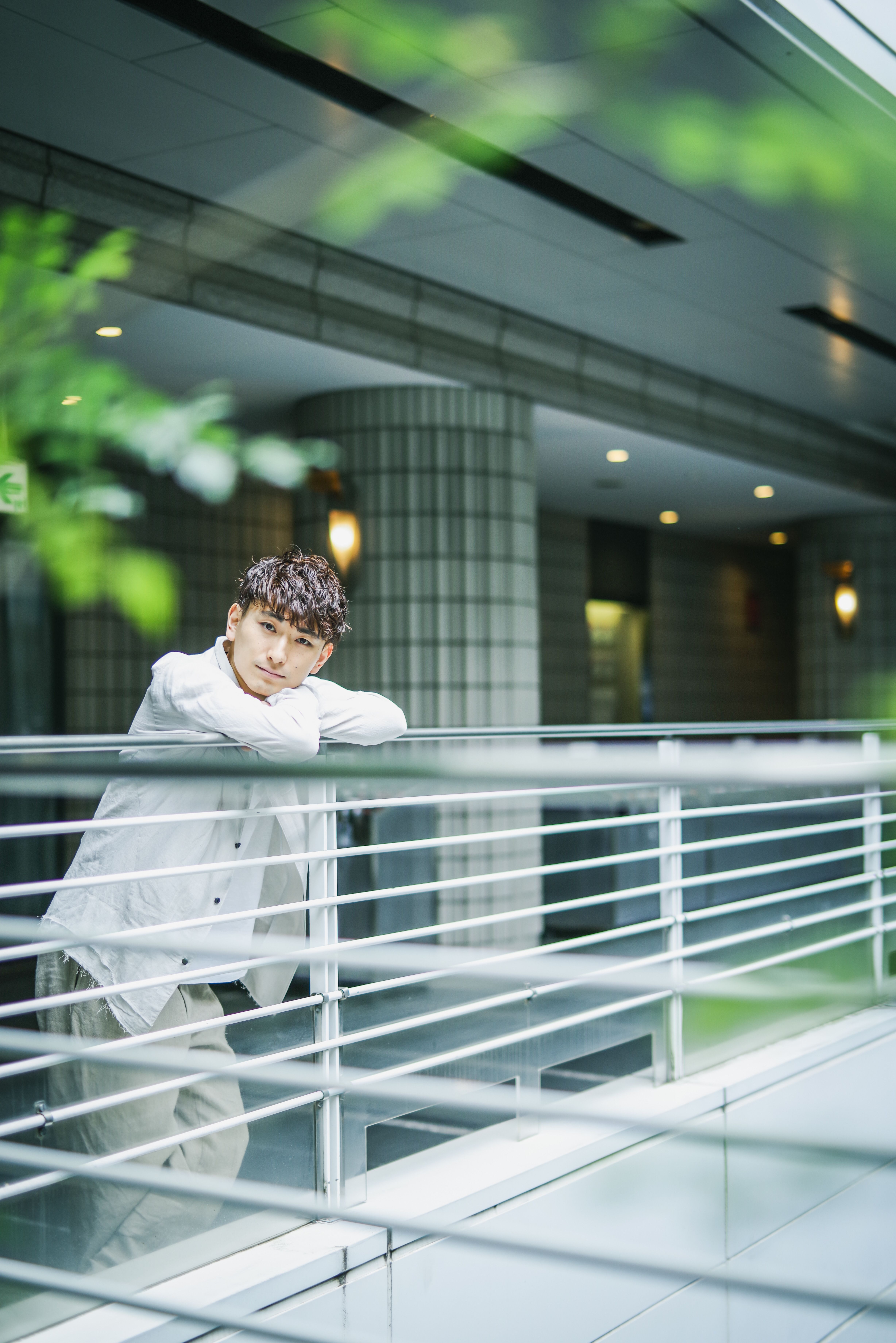 Asian man in stylish casual attire posing indoors by metal handrails.