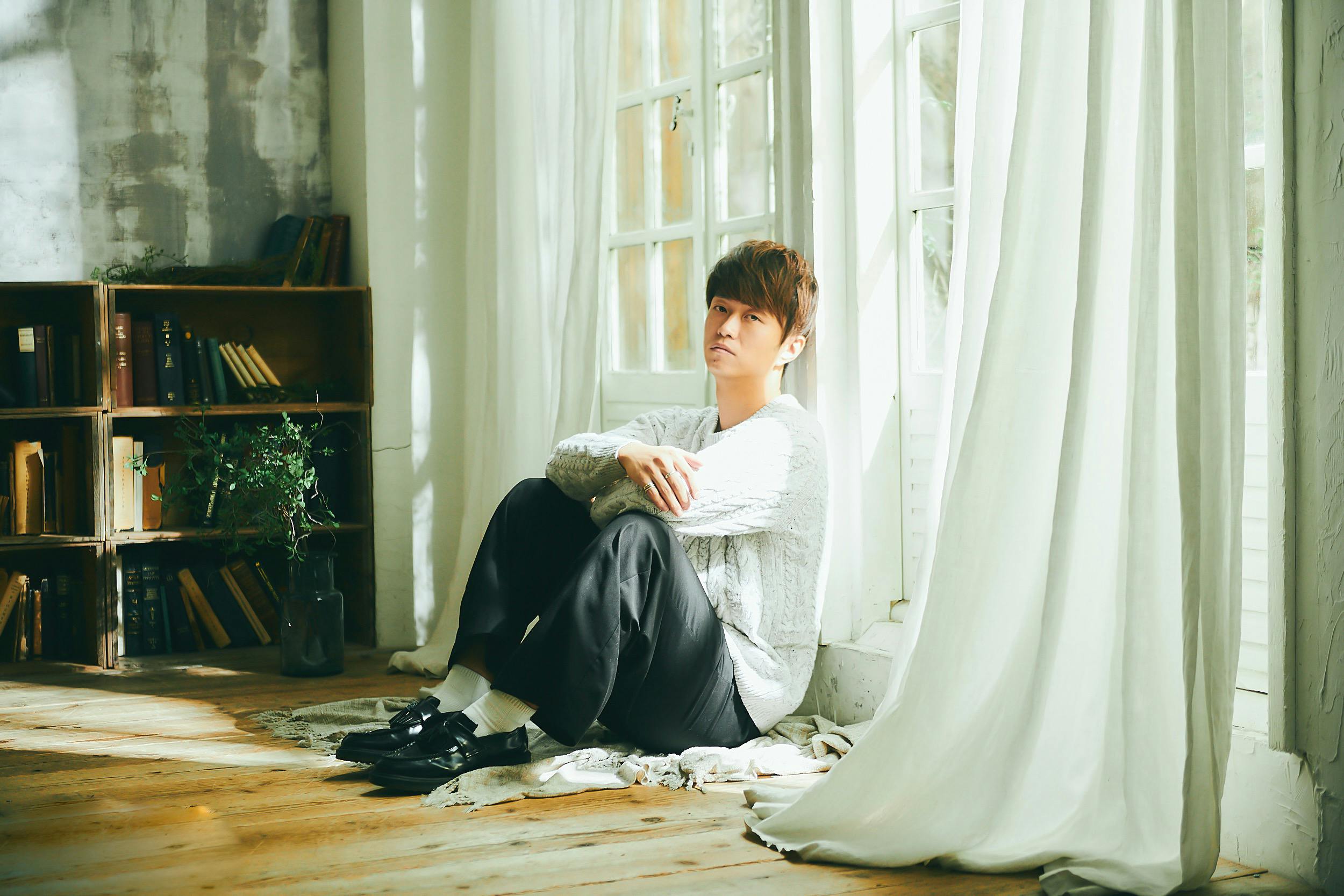 A fashionable man sits thoughtfully by a sunlit window in a cozy room.
