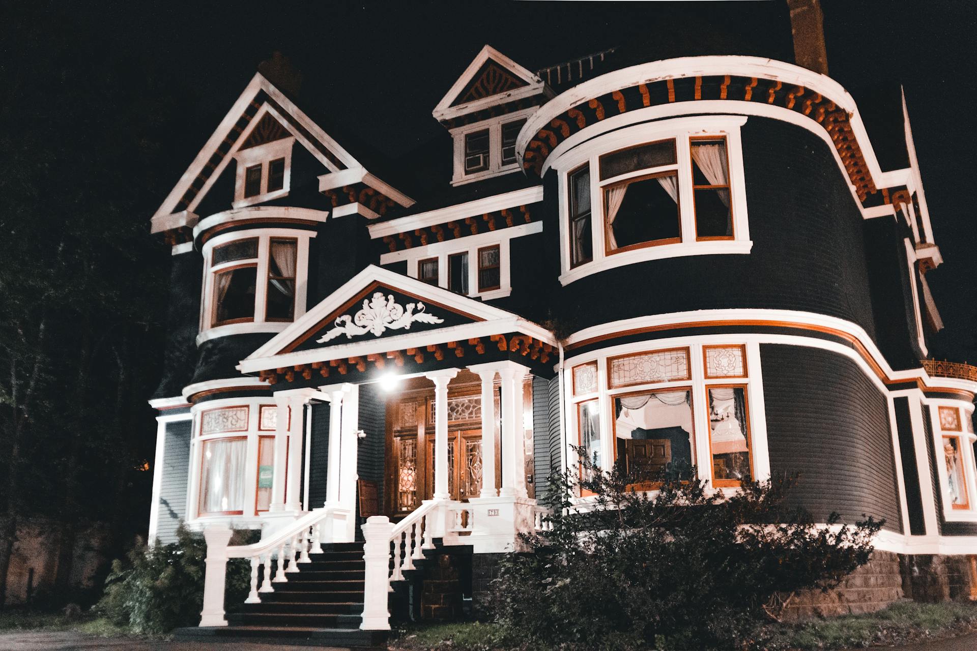 Capture of a grand Victorian mansion exterior illuminated at night, showcasing intricate architectural details.