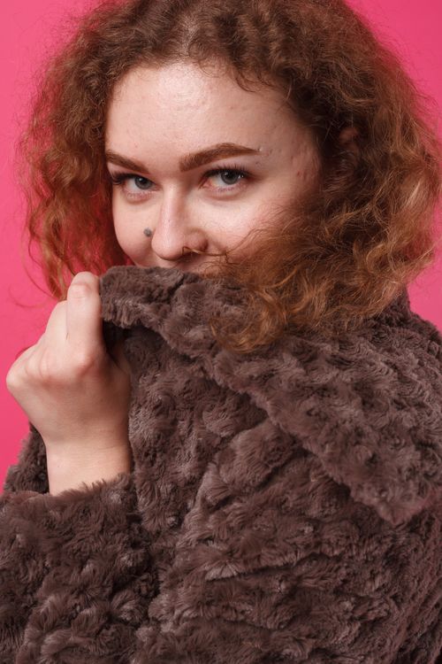 Free Close-up portrait of a woman in a fur coat against a vibrant pink background, expressing warmth. Stock Photo