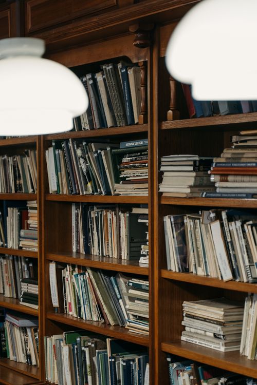 Free Wooden bookshelves filled with books under soft overhead lighting in a cozy library setting. Stock Photo