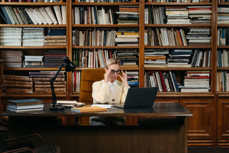 A woman working on her laptop in a library room with shelves