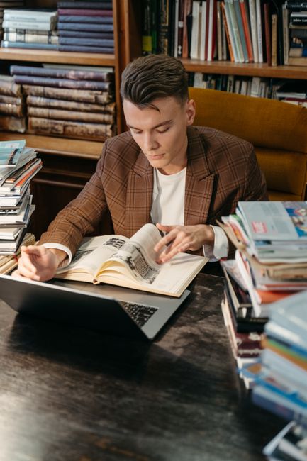 A young man studying diligently with books and a laptop in a library setting. A young man studying diligently with books and a laptop in a library setting.