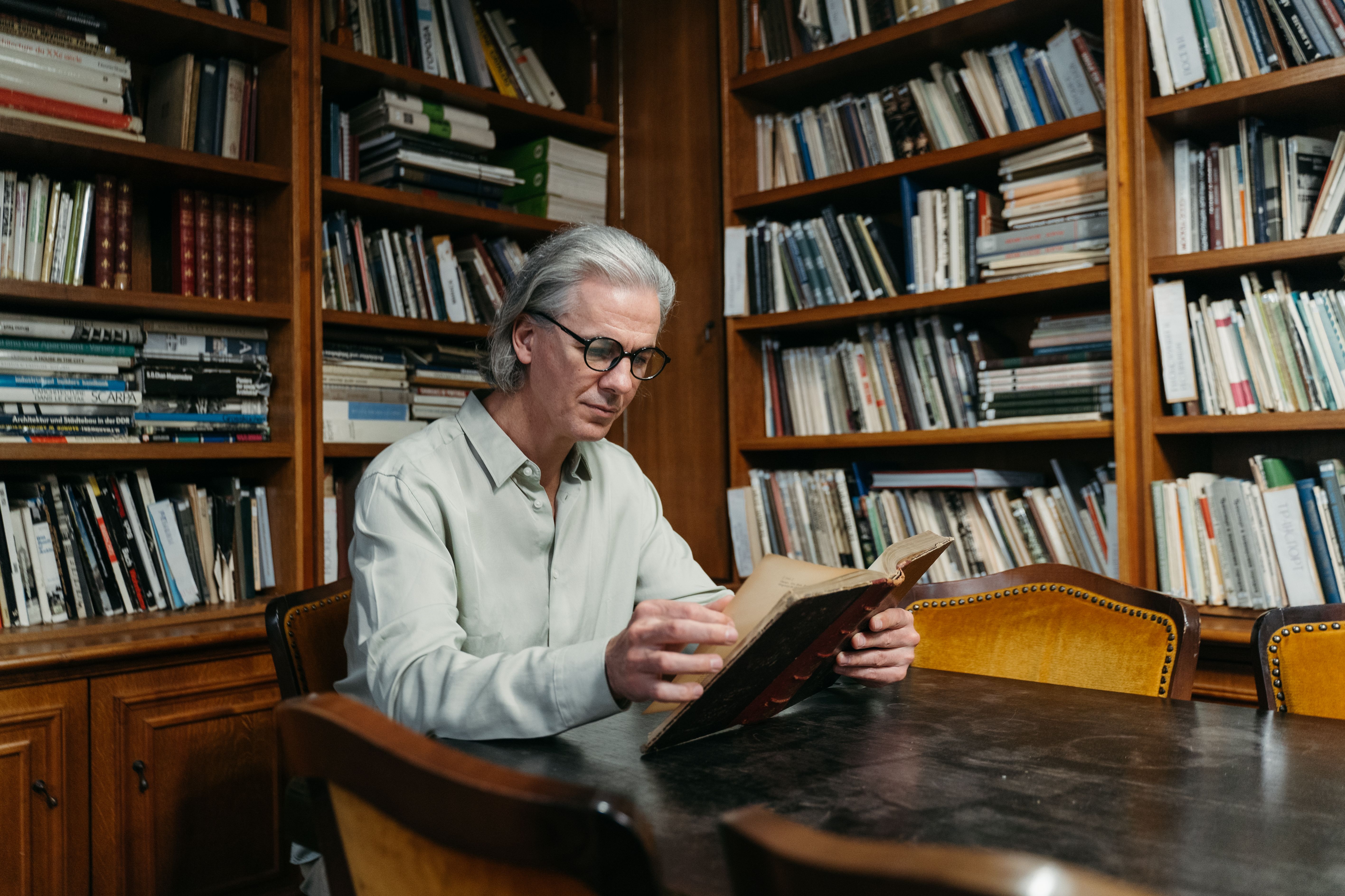 Elderly man engrossed in reading in a peaceful library full of books.