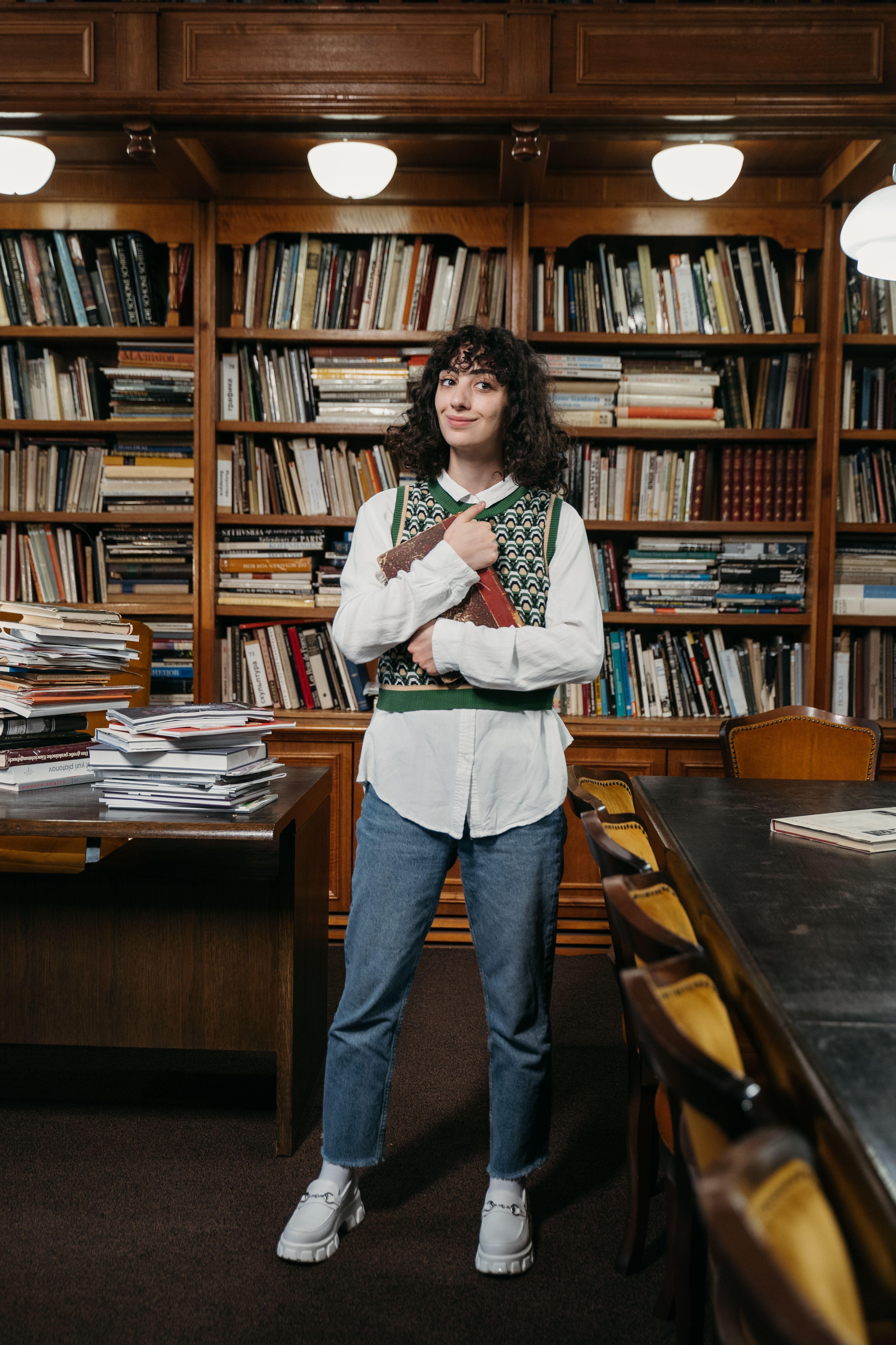 Woman in forest green sweater vest over white shirt with jeans