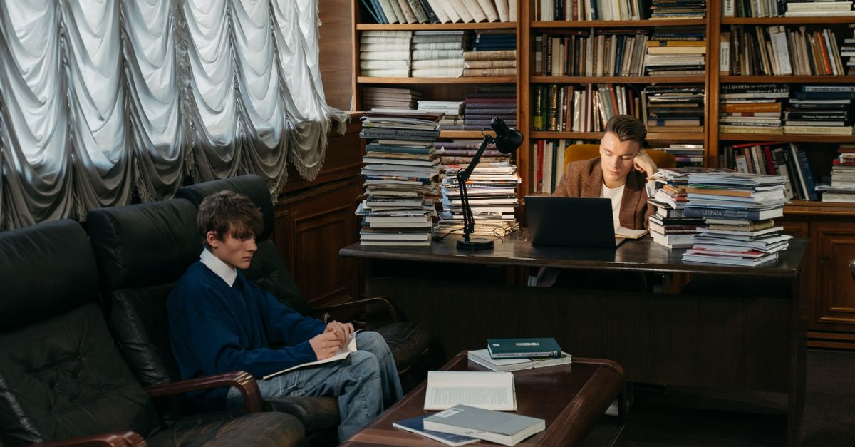 Two college students studying in a cozy library with books and laptop, reflecting academic life.