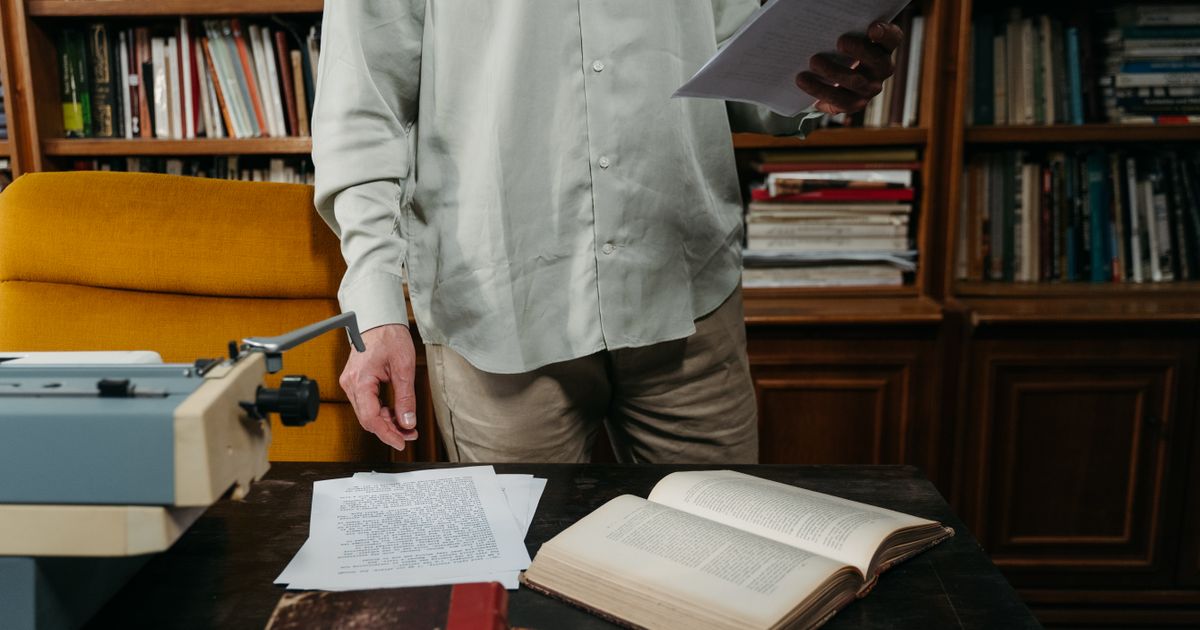 Man reviewing documents in a cozy library with books, papers, and typewriter.