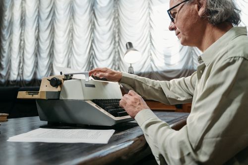 Free Adult man typing on a vintage mechanical typewriter at a desk indoors. Stock Photo