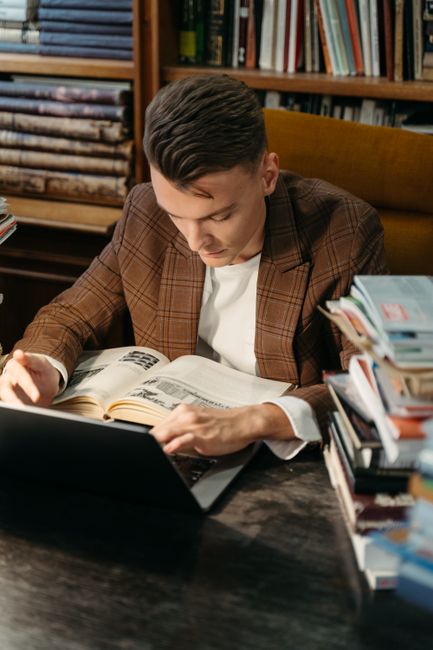 A young man reading at a library desk surrounded by books, focusing on education. A young man reading at a library desk surrounded by books, focusing on education.