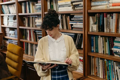 Free A young woman reading inside a library, surrounded by shelves of books, ideal for education themes. Stock Photo