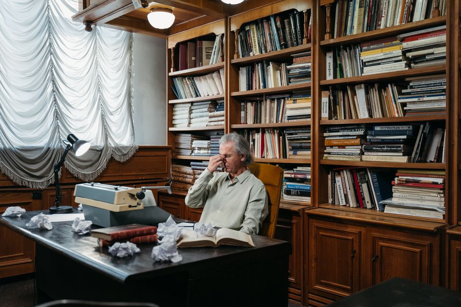 Senior man tired at desk with typewriter and books in a classic office setting.