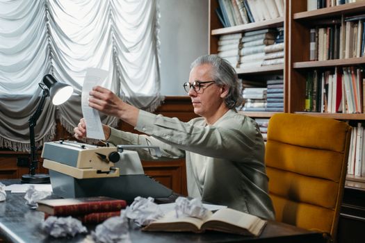 Elderly Man Sitting on Chair while Holding a Paper in the Library