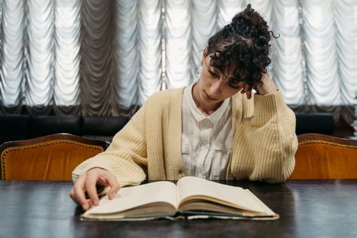 Free A woman deeply engaged in reading a book at a table, capturing a serene learning moment. Stock Photo